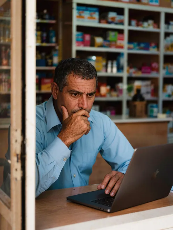 Dono de farmácia preocupado olhando as vendas no notebook